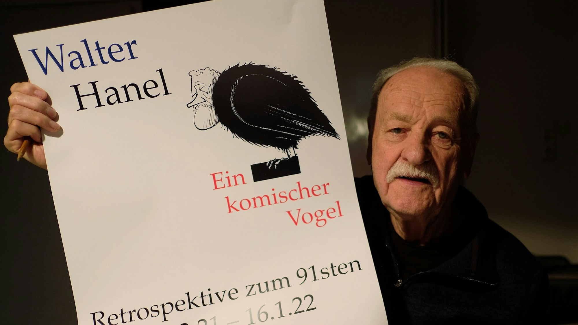 Walter Hanel hält ein Ausstellungsplakat in die Höhe.
