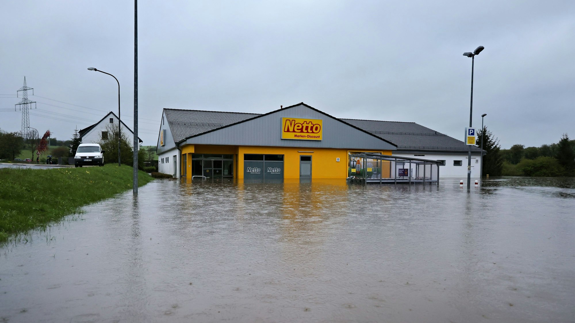 Das Bild zeigt den Netto-Markt von außen. Von vorne und von der rechten Seite ist er von Wasser umgeben.