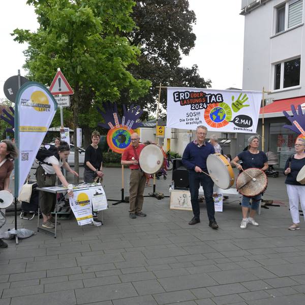 Mitglieder der Initiativen stehen vor Plakaten und trommeln, um auf ihre Veranstaltung aufmerksam zu machen.