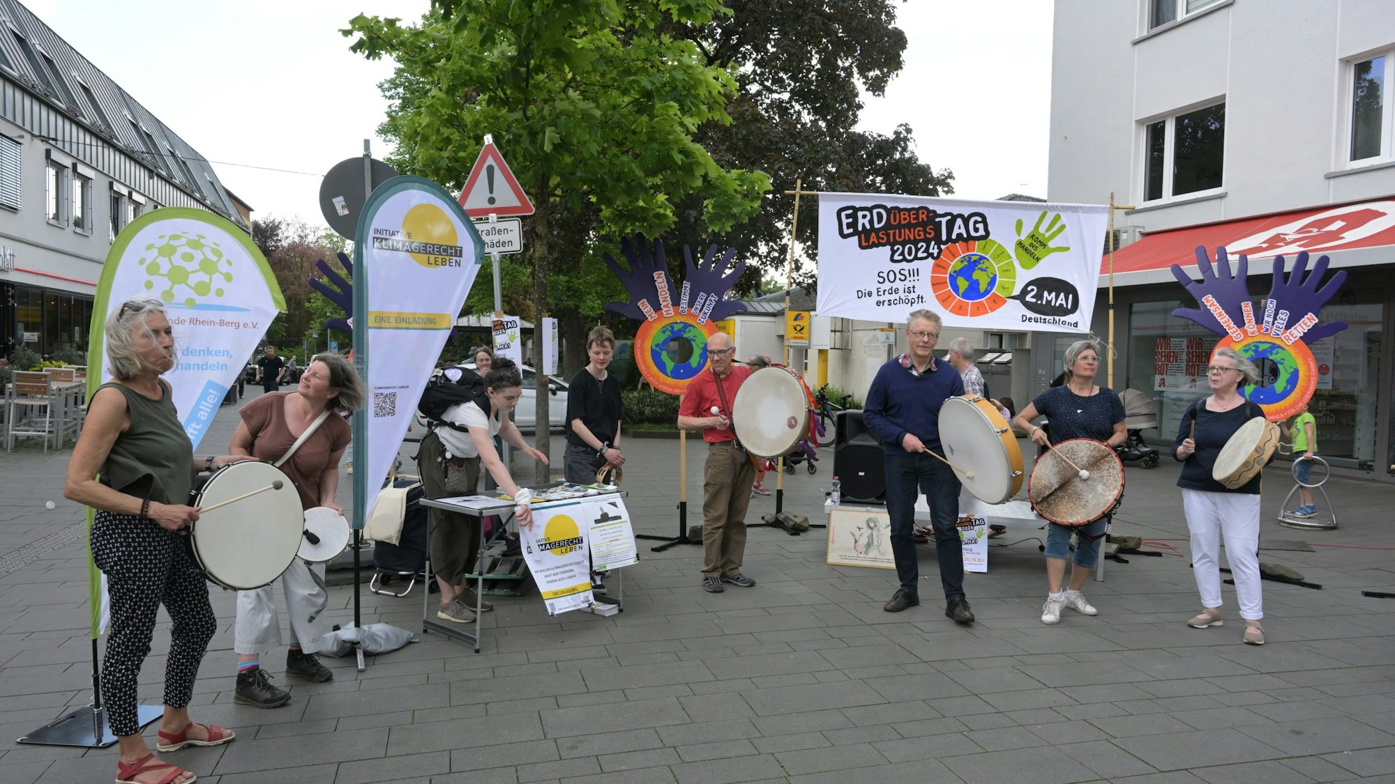 Mitglieder der Initiativen stehen vor Plakaten und trommeln, um auf ihre Veranstaltung aufmerksam zu machen.