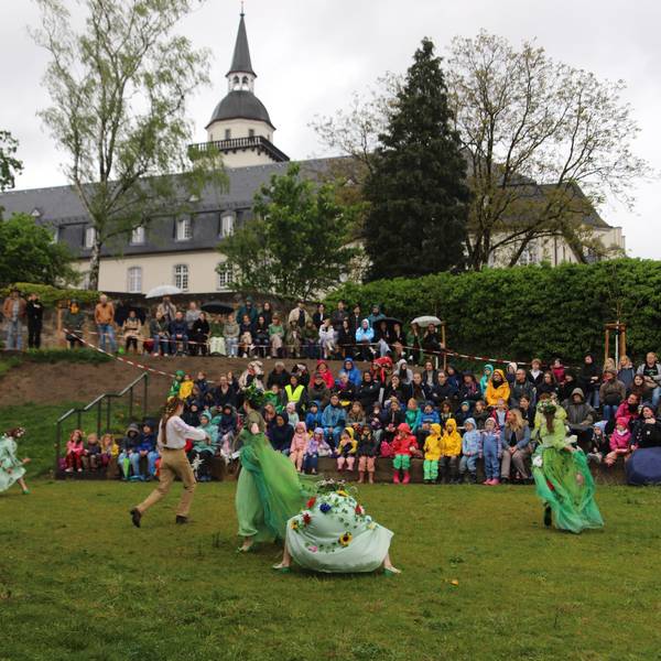 Die Feen tanzen im Johannisgarten vor ihrem Publikum, mit der ehemaligen Abtei im Hintergrund.