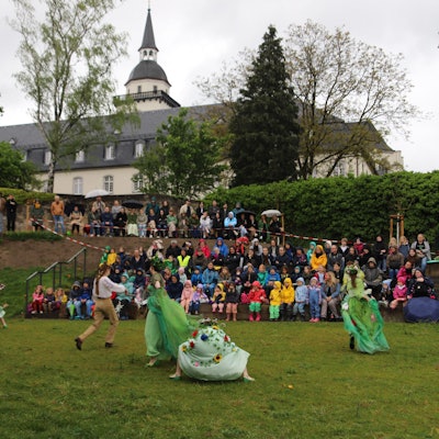 Die Feen tanzen im Johannisgarten vor ihrem Publikum, mit der ehemaligen Abtei im Hintergrund.
