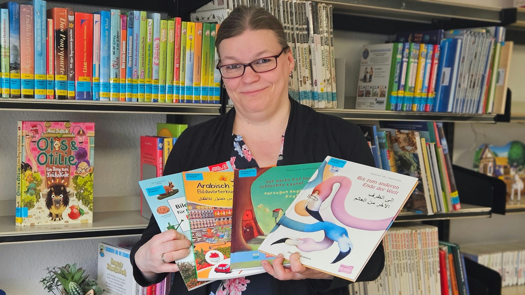 Eine Frau steht vor einem Bücherregal und hält mehrere zweisprachige Kinderbücher.