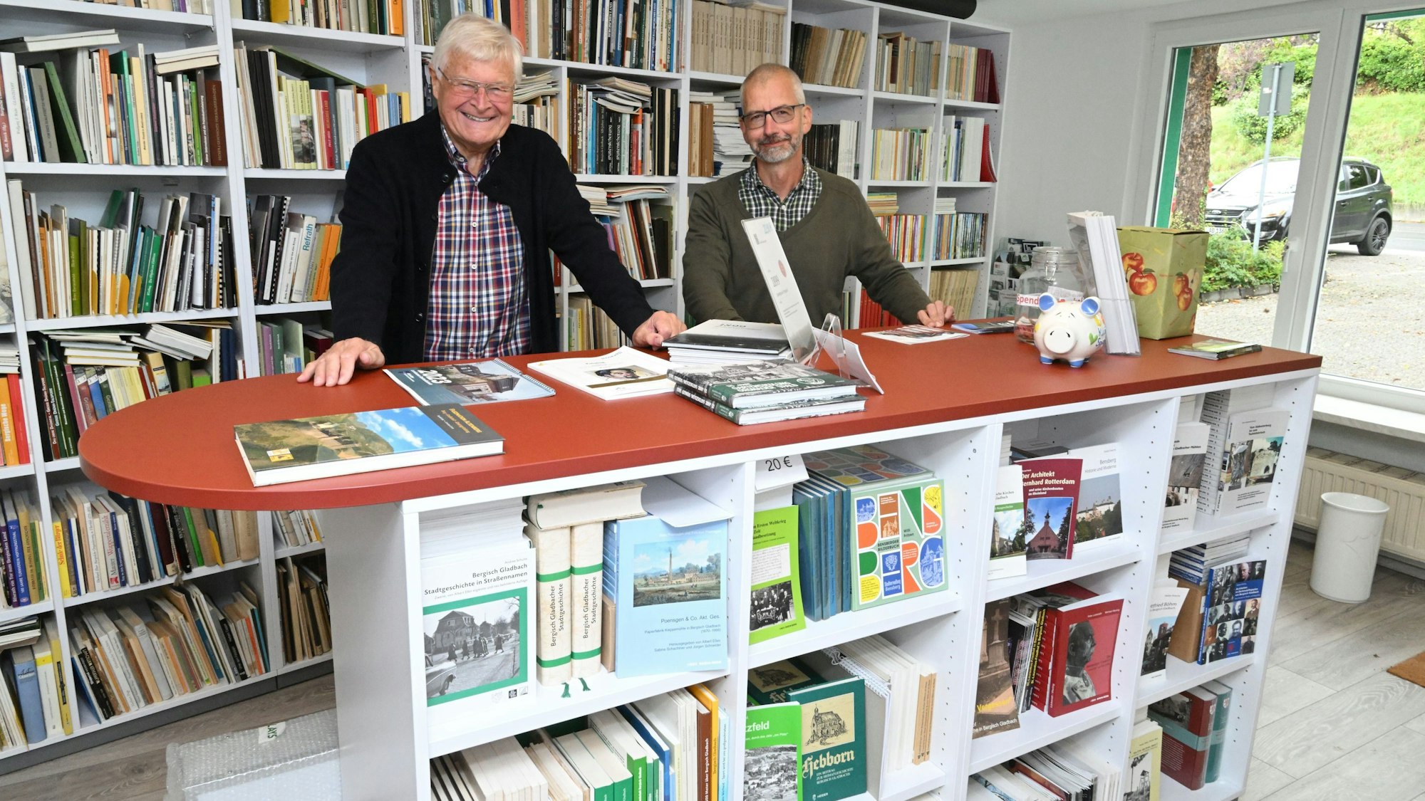 Zwei Männer stehen hinter einem Tresen, der gefüllt ist, mit historischen Büchern. Hinter ihnen stehen gefüllte Bücherregale.