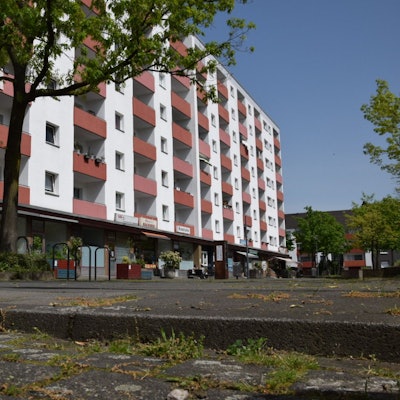 Blick auf den Piccoplatz in Köln-Holweide, der nicht barrierefrei ist. Im Hintergrund ist ein Hochhaus zu sehen. Foto von Rika Kulschewski.