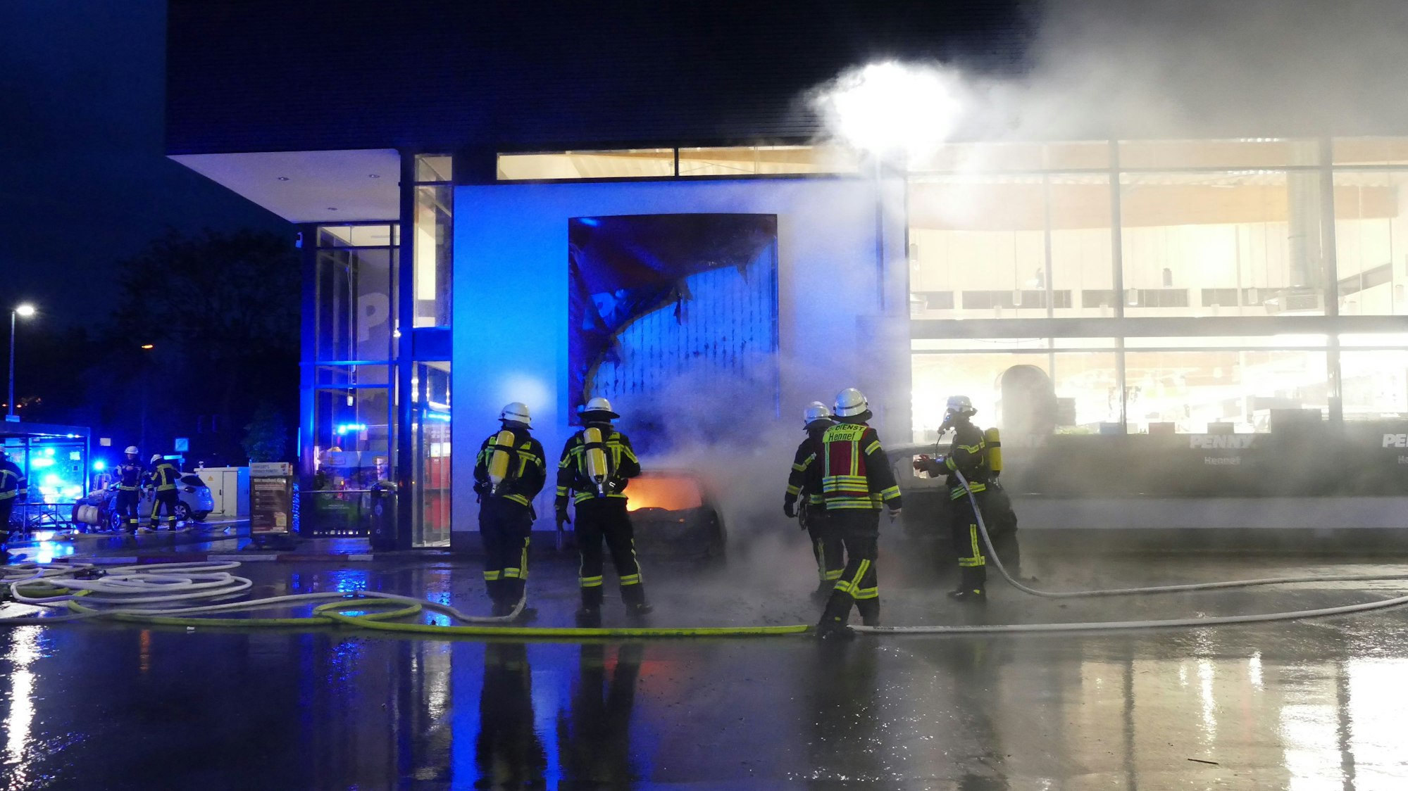 Zwei brennende Autos stehen vor einem Supermarkt.
