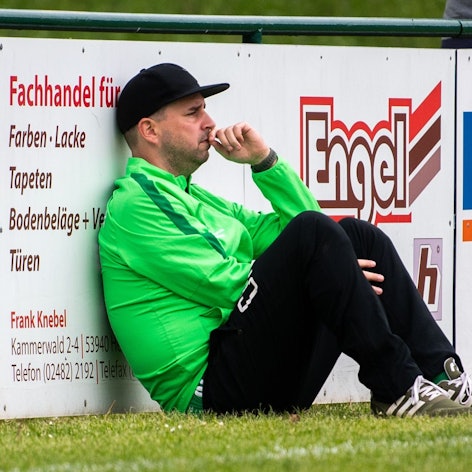 Das Bild zeigt Sötenichs Trainer an einer Bande sitzend.