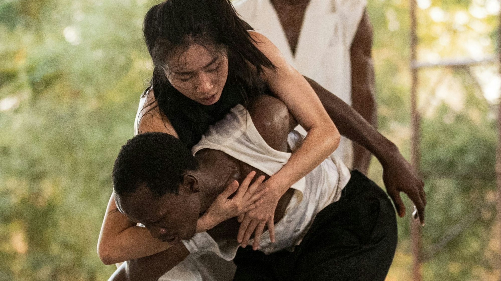 Auf dem Bild sind ein Tänzer und eine T#nzerin zu sehen, in schwarz-weißer Kleidung. Die Tänzerin umklammert den Tänzer mit ihren Händen, er ist in geduckter Haltung.