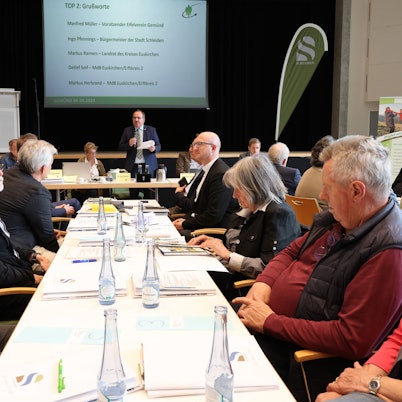 Zahlreiche Personen sitzen bei der Tagung des Eifelvereins im Kursaal Gemünd an Tischen. In der Mitte steht Hauptvorsitzender Dr. Ralf Nolten.