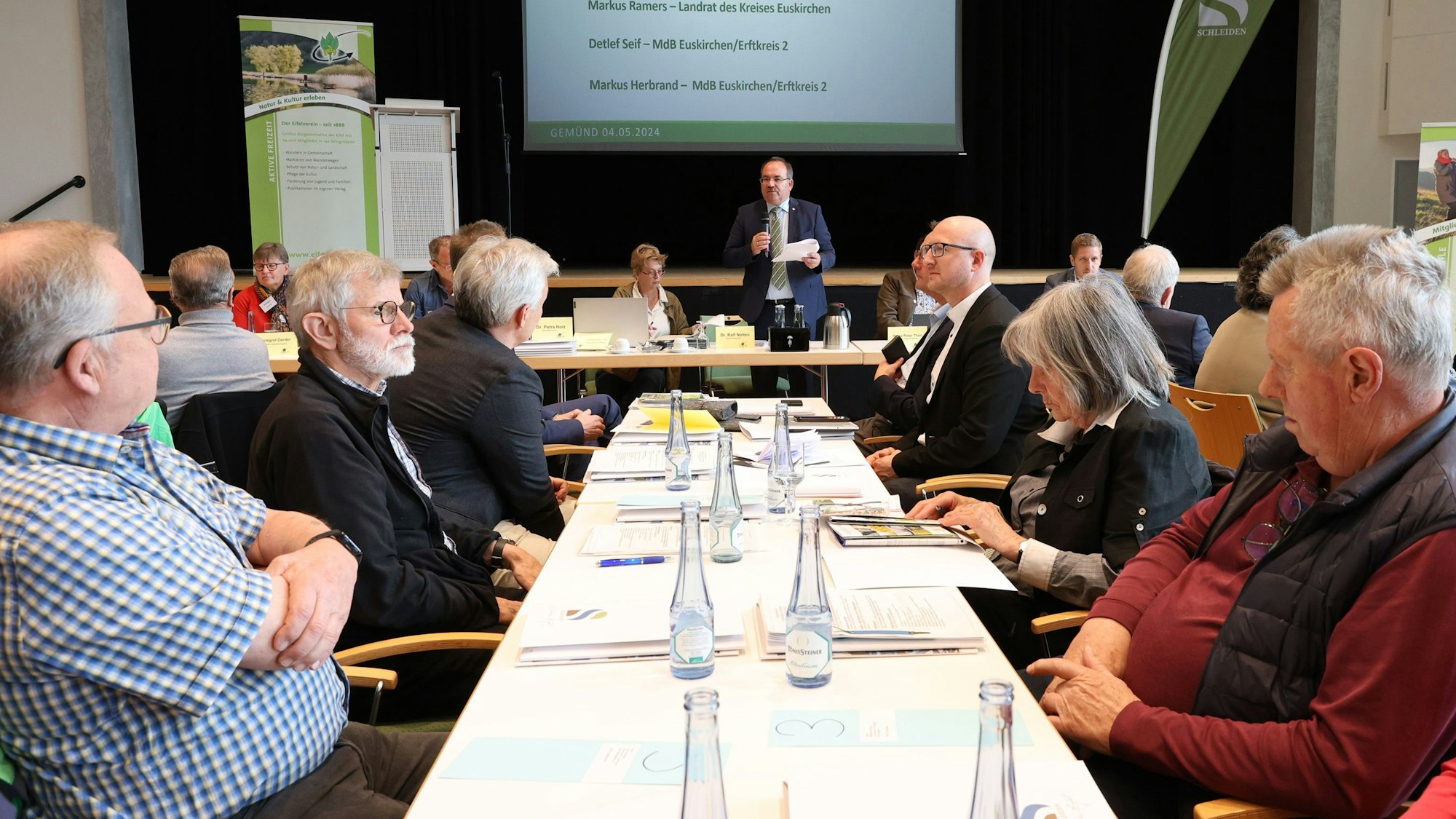 Zahlreiche Personen sitzen bei der Tagung des Eifelvereins im Kursaal Gemünd an Tischen. In der Mitte steht Hauptvorsitzender Dr. Ralf Nolten.