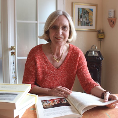 Zu sehen ist die Historikerin Claudia Wendels an einem Tisch sitzend in der Vorderansicht. Auf dem Tisch liegen mehrere Bücher.