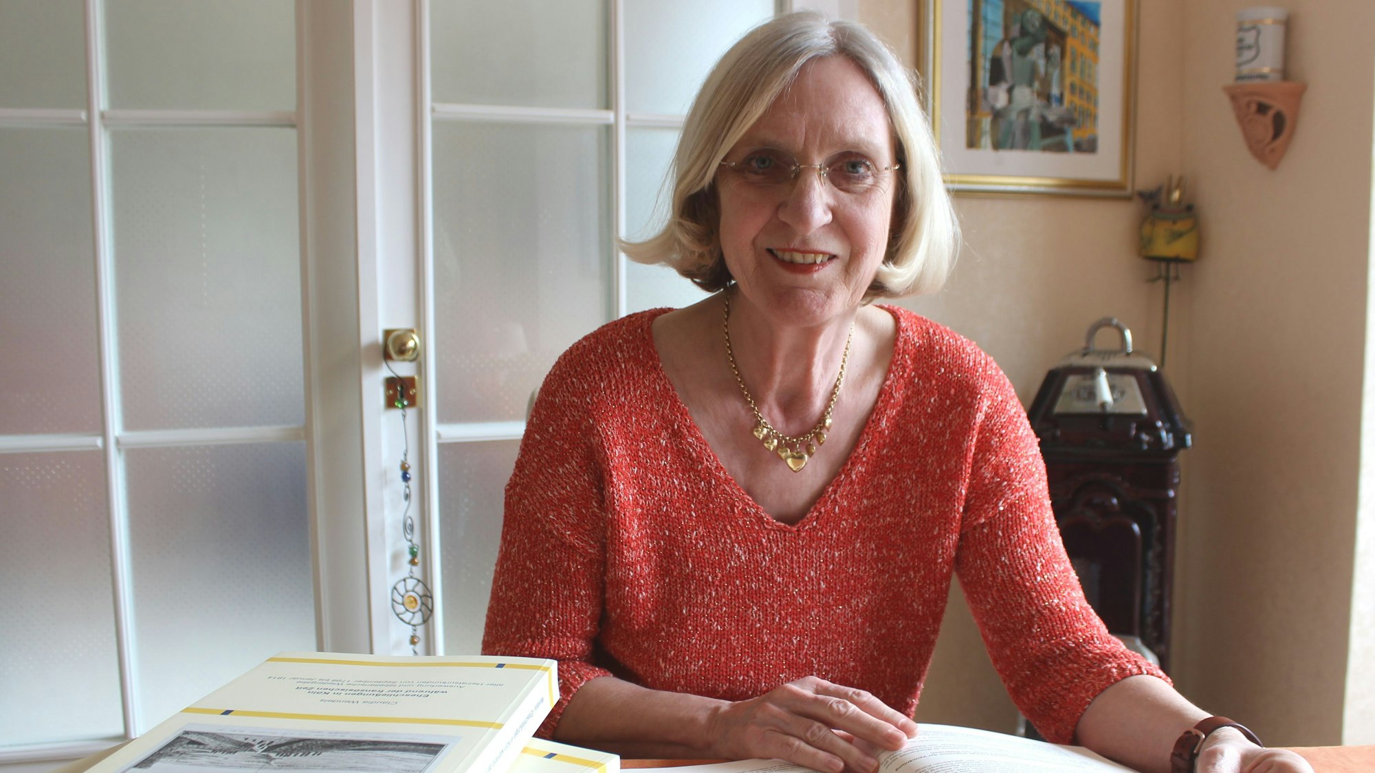 Zu sehen ist die Historikerin Claudia Wendels an einem Tisch sitzend in der Vorderansicht. Auf dem Tisch liegen mehrere Bücher.