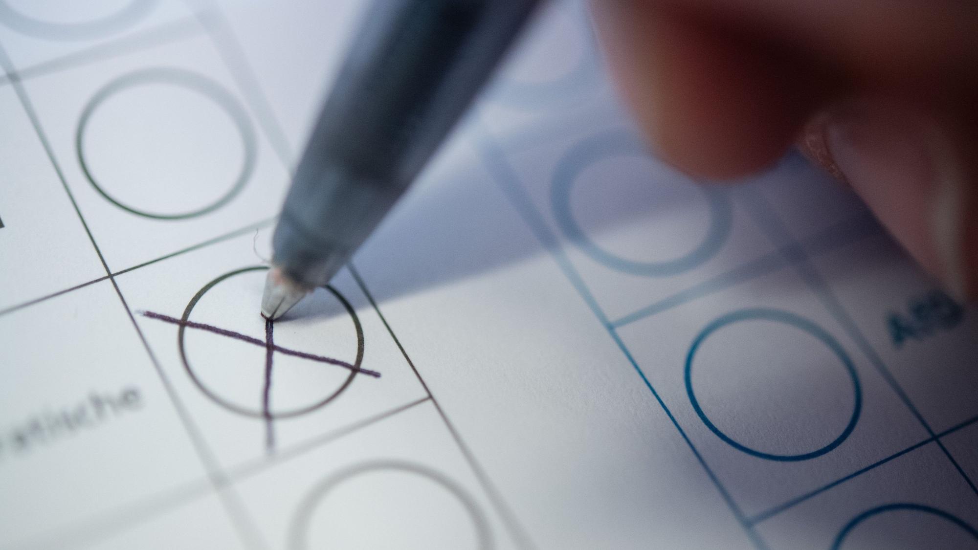 Eine Hand hält einen Stift und setzt ihr Kreuz auf einem Wahlzettel.