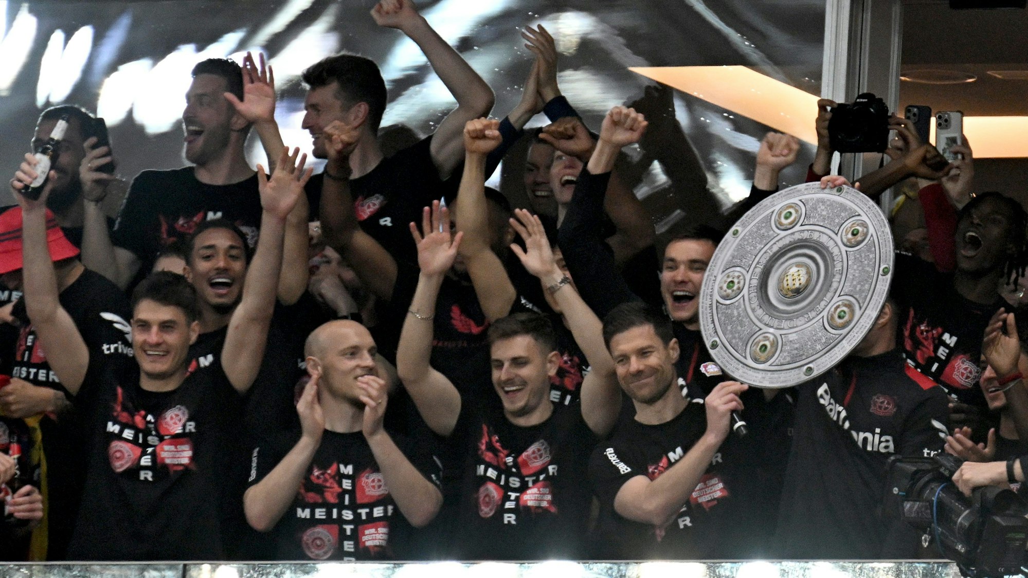 Die Leverkusener Mannschaft um Trainer Xabi Alonso jubelt mit einer stilisierten Meisterschale von der Tribüne ins Stadion