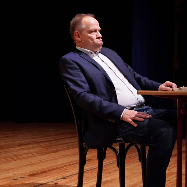 Kabarettist Thomas Schreckenberger sitzt im Stadttheater in Euskirchen an einem Tisch. Er gibt eine gelungene Version von Klaus Kinski zum besten.