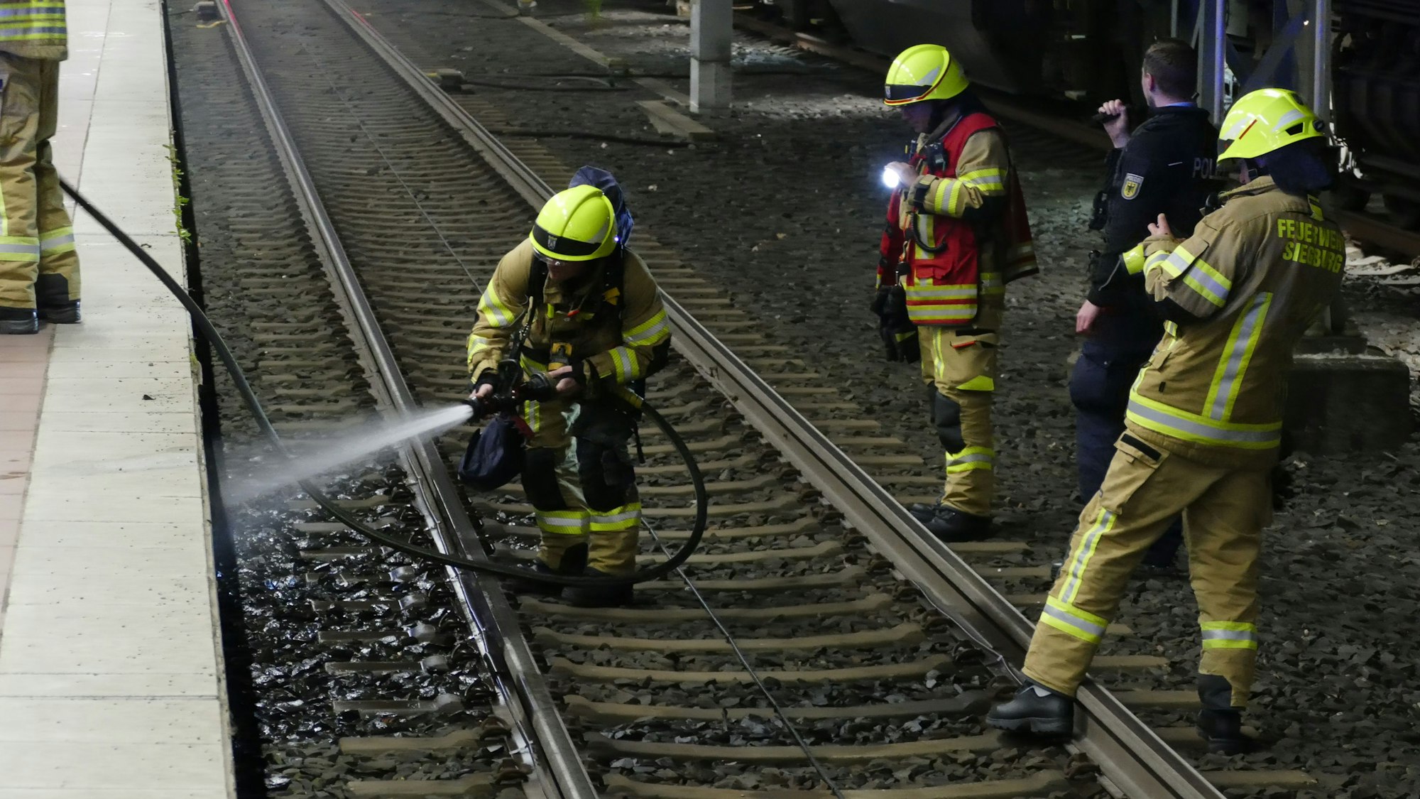 Feuerwehrleute stehen auf Schienen.