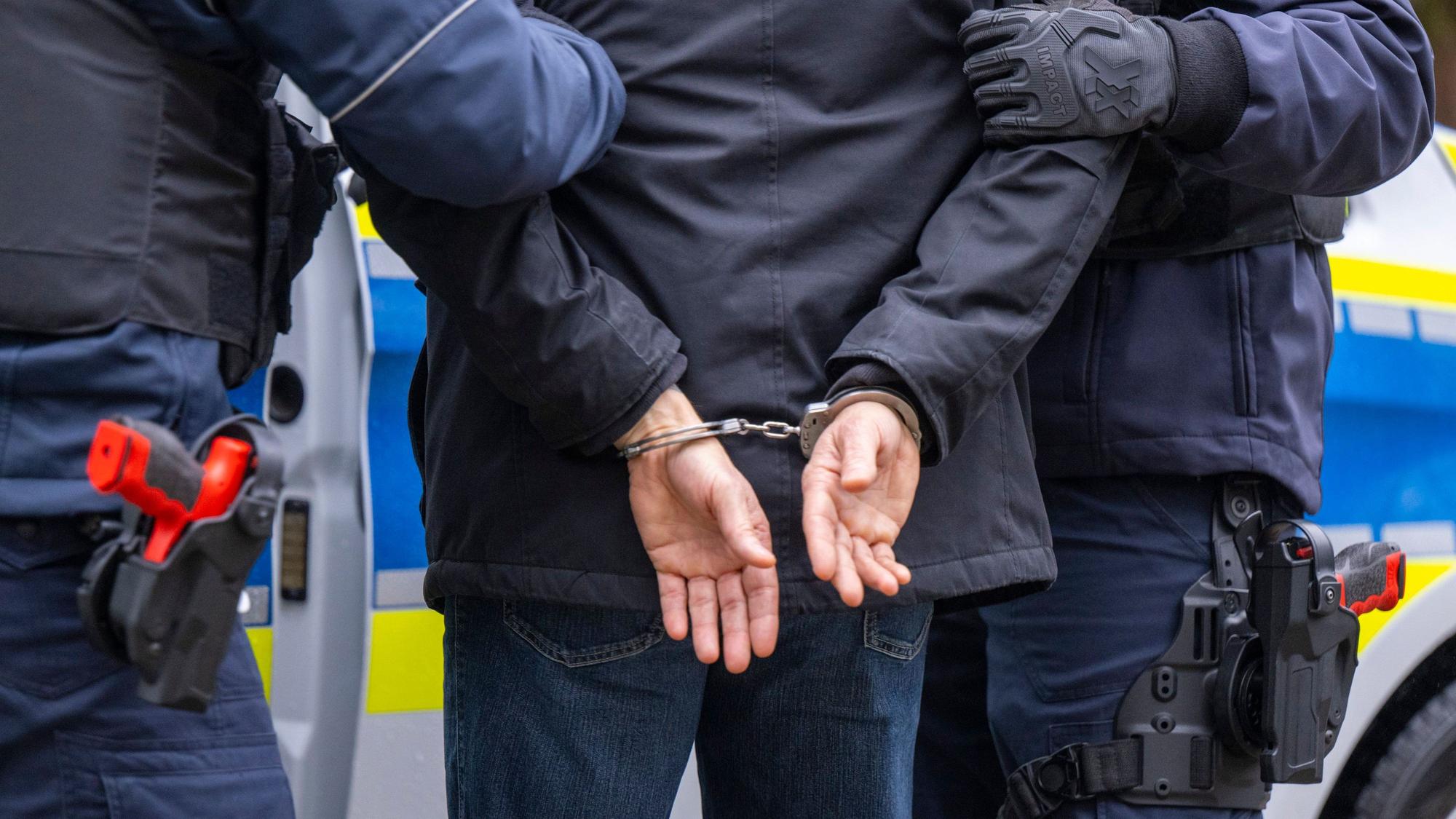Zwei Polizisten führen einen Mann in Handschellen ab