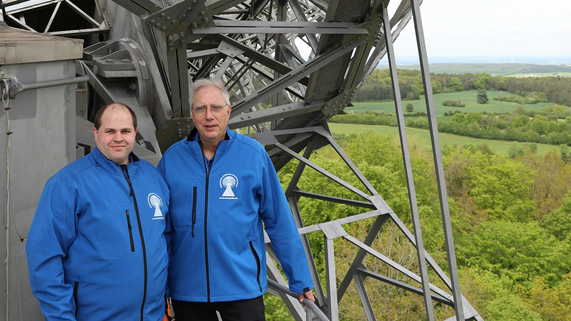 Kevin Schmitz (l.) und Walter Grode stehen auf der Arbeitsplattform der Radioteleskopschüssel, rechts ist der Blick in die Weite der Eifellandschaft zu sehen.