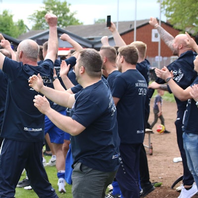 Fußballfans jubeln am Spielfeldrand.