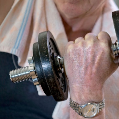 Das Foto zeigt einen älteren Menschen, der eine Hantel stemmt.