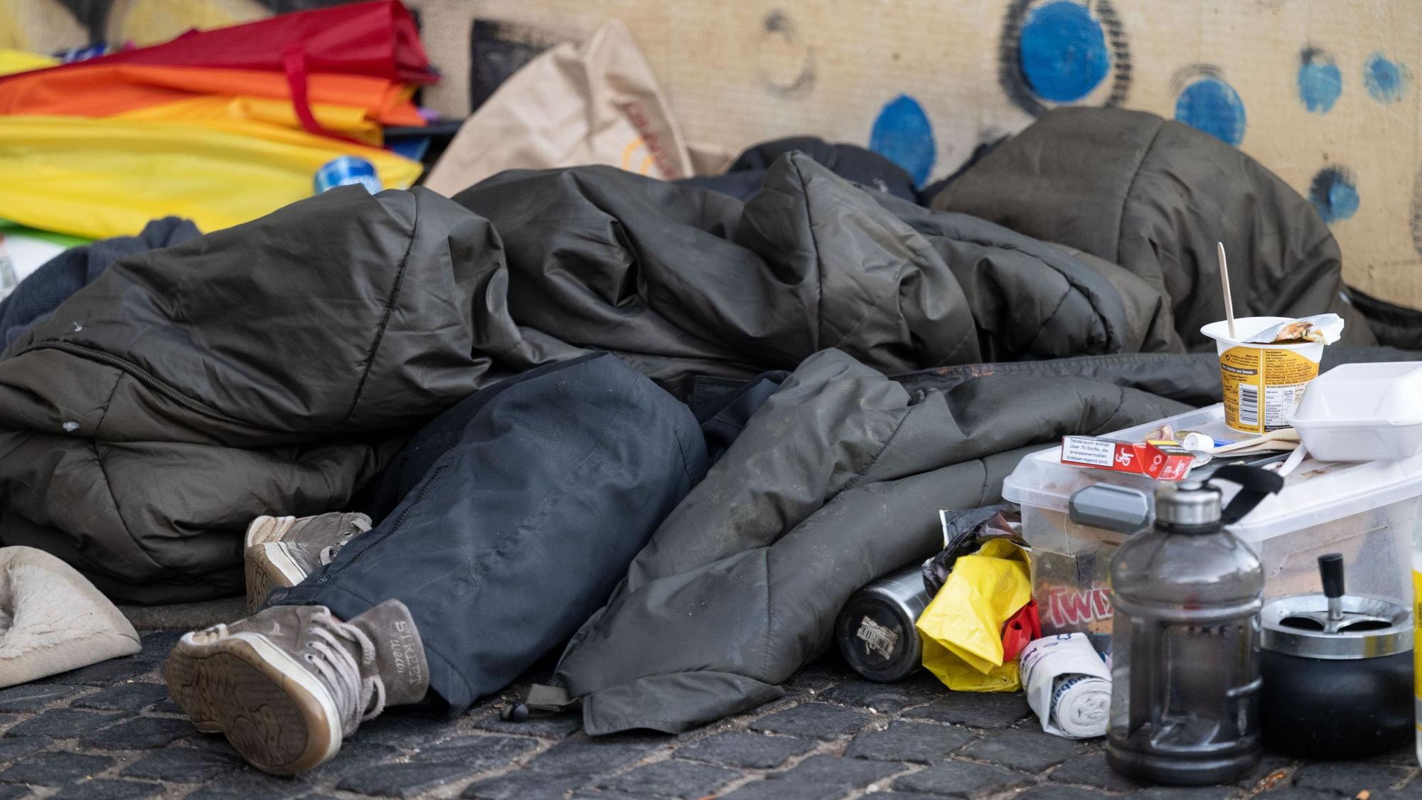 Eine Person liegt in der Innenstadt unter einem Schlafsack.