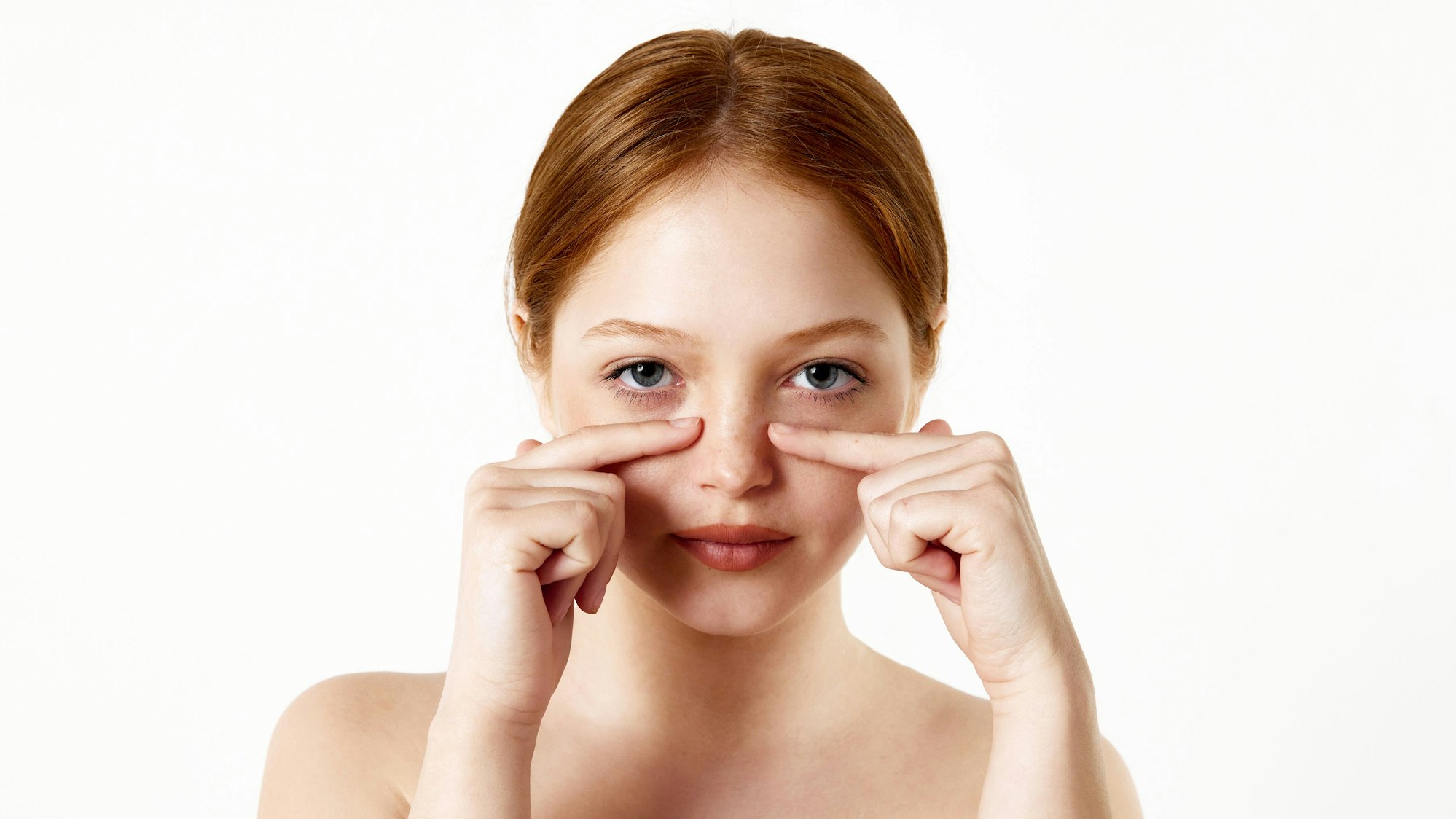 Portrait of tender, beautiful, young redhead girl touching nose against white studio background. Rhinoplasty, nose surgery. Concept of beauty, plastic surgery, rhinoplasty, cosmetology, health