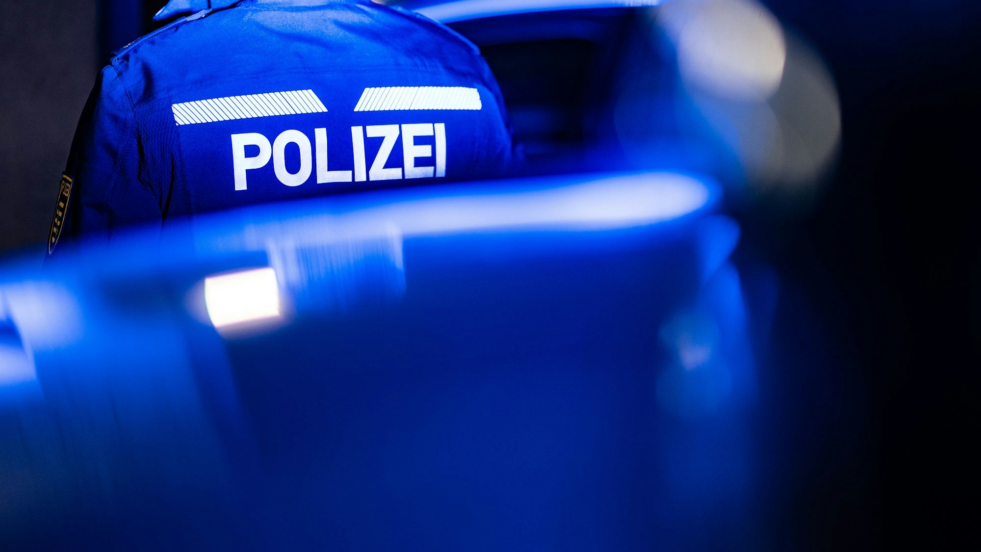 Ein Polizist steht neben einem Polizeifahrzeug.
