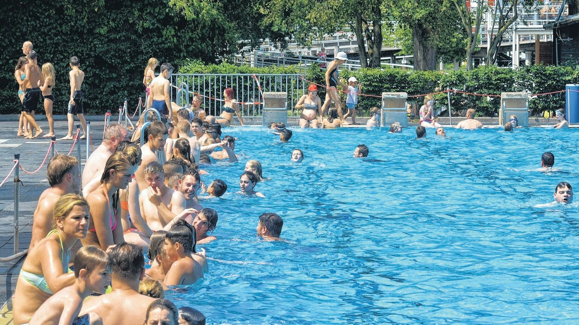 Ein Schwimmbecken. Am Rand sitzen viele Menschen.