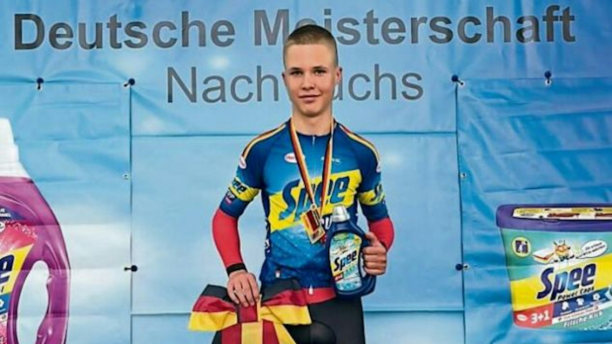 Radrennfahrer Mika Lohmar steht mit einer schwarz-rot-goldenen Siegerschleife auf dem Treppchen.