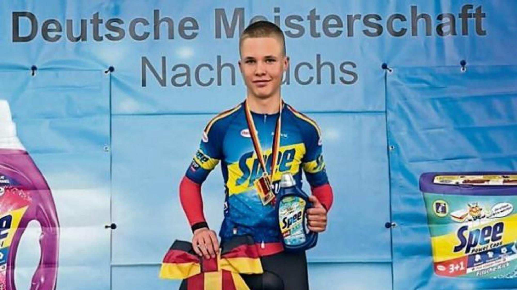 Radrennfahrer Mika Lohmar steht mit einer schwarz-rot-goldenen Siegerschleife auf dem Treppchen.
