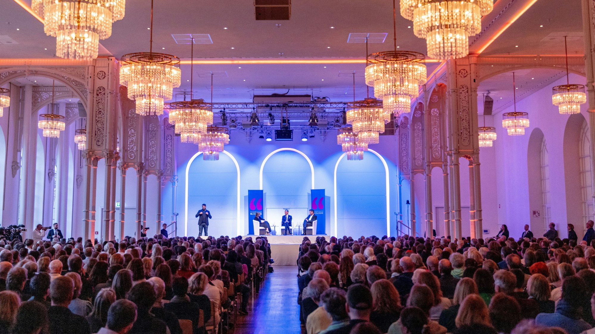 Innenansicht mit Kronleuchtern und Menschen im Publikum