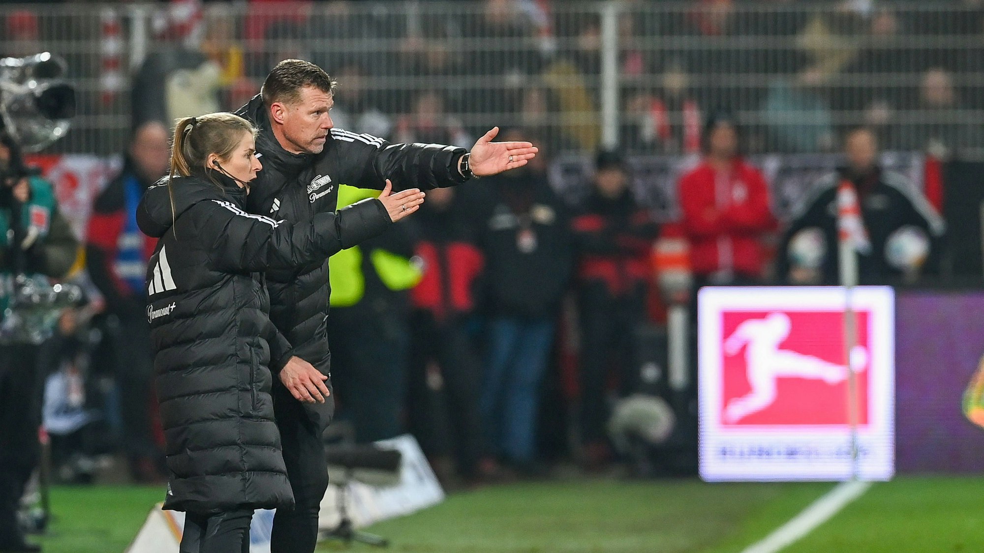 Union Berlins Interimstrainer Marco Grote mit seiner Assistentin Marie-Louise Eta beim Bundesligaspiel gegen Augsburg im November 2023. Beide zeigen auf den Platz und beraten sich augenscheinlich zum Spiel.
