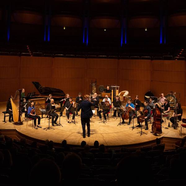 Auf der Bühne der Philharmonie steht das Ensemble mit einem Flügel, einer Harfe, Perkussion, Streichern und Bläsern. Vorne steht der Dirigent Enno Poppe, dem Ensemble zugewandt.