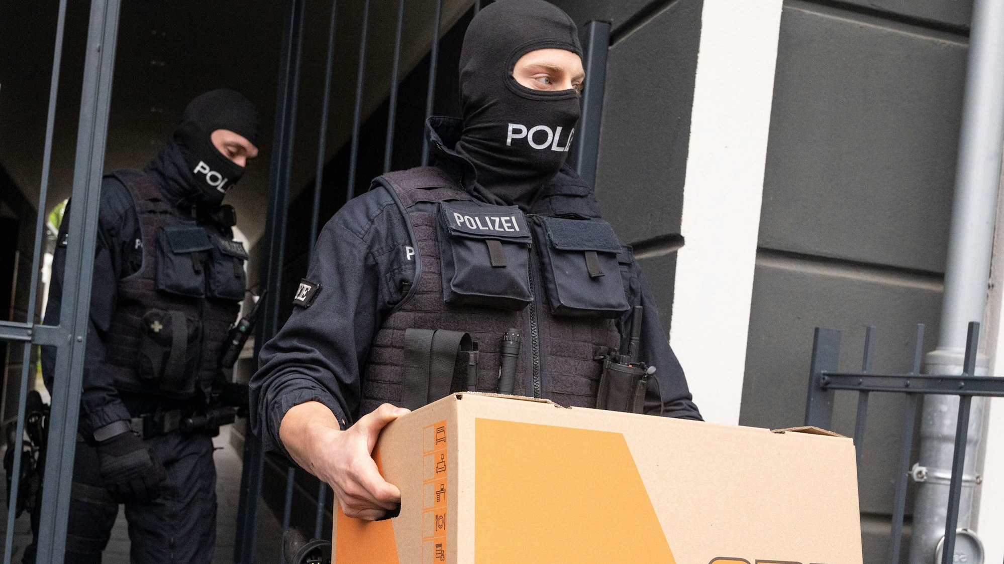 Ein Polizist trägt im Rahmen einer Razzia gegen Schleuser ein Karton aus einem Gebäude.
