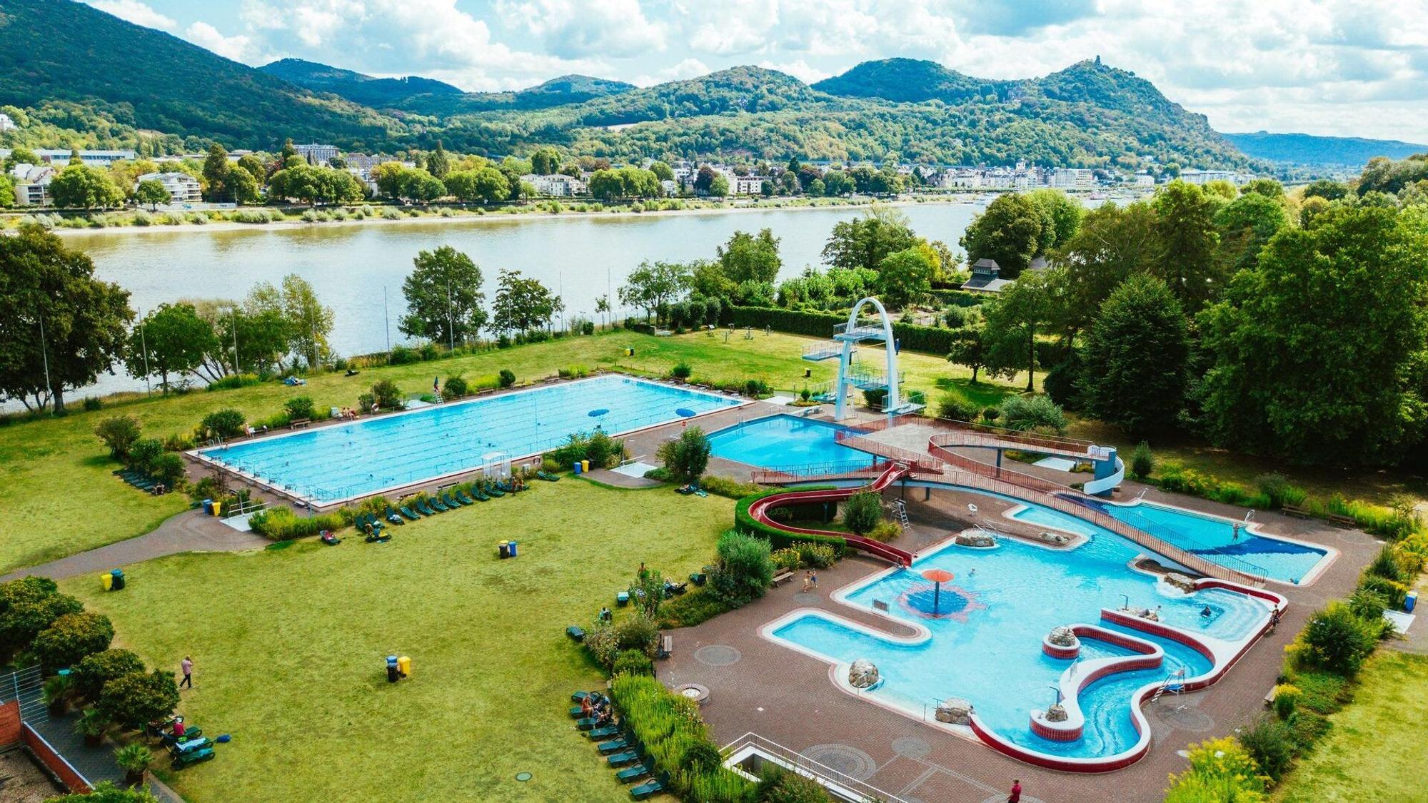 Ein Luftbild des Freibads Rüngsdorf mit seinen verschiedenen Becken. Im Hintergrund ist der Rhein zu sehen, der am Schwimmbad vorbeifließt.