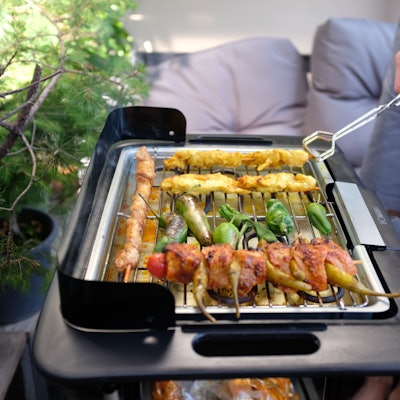 Ein Mann, der eine Grillzange hält, brät auf seinem Balkon mithilfe eines Elektrogrills Fleisch und Gemüse