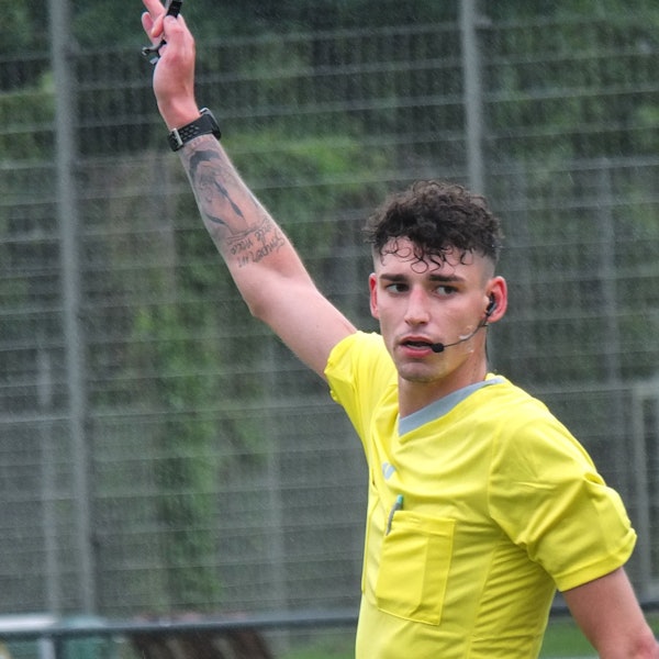 Pascal Kaiser hebt eine Hand, er trägt ein gelbes Schiedsrichter-Shirt.