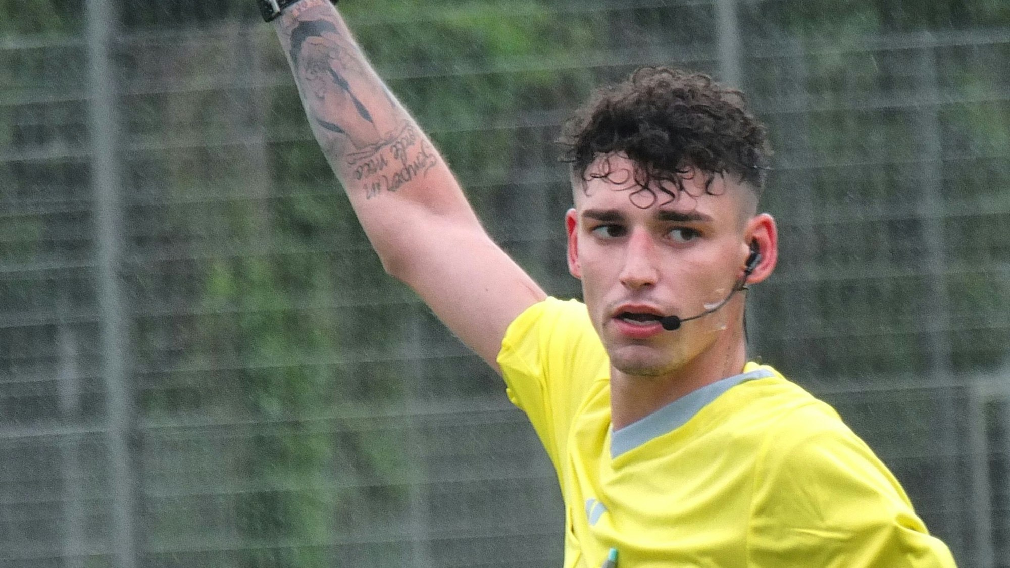 Pascal Kaiser hebt eine Hand, er trägt ein gelbes Schiedsrichter-Shirt.