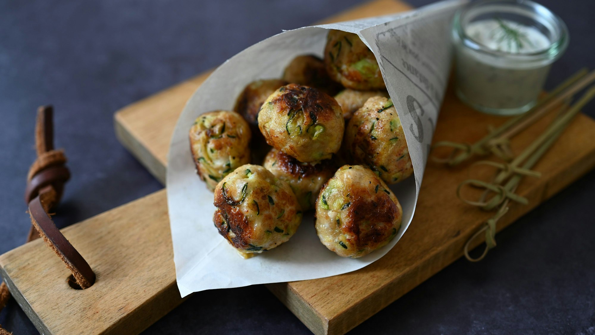 Die kleinen Zucchini-Hähnchen-Bällchen liegen in einer spitzen Papiertüte auf einem Brettchen.