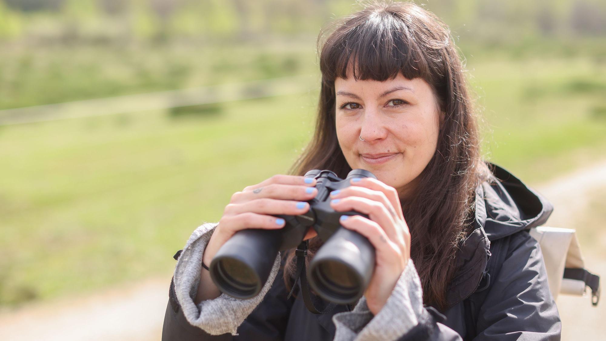 Jana Romero macht in ihrer Freizeit gerne Birdwatching. Porträt von ihr mit Fernglas in der Wahner Heide.