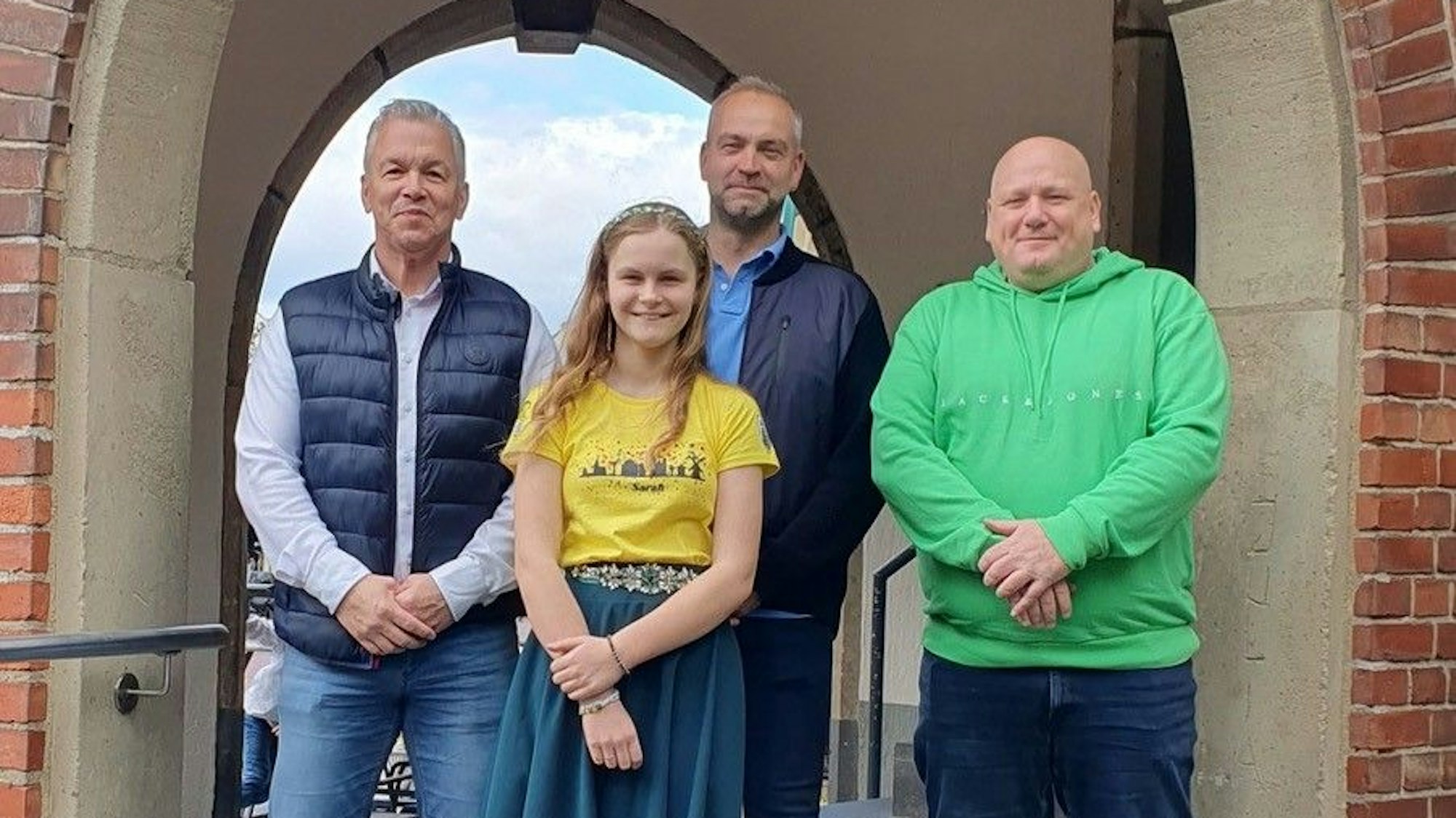 Drei Männer und ein Mädchen stehen in einem Torbogen und lächeln.