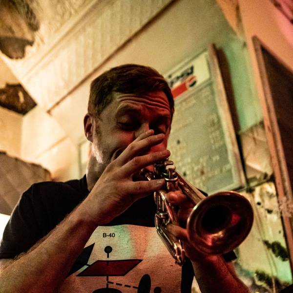 Peter Evans spielt seine Trompete. Es ist eine Nahaufnahme. Er trägt ein schwarzes T-Shirt mit einem weißen Bild darauf.