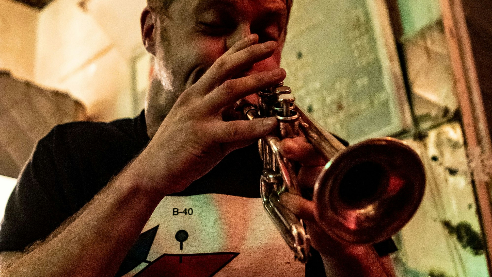 Peter Evans spielt seine Trompete. Es ist eine Nahaufnahme. Er trägt ein schwarzes T-Shirt mit einem weißen Bild darauf.