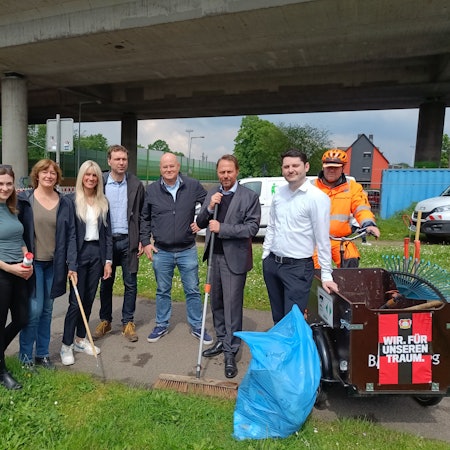 Vier Frauen und fünf Männer posieren zusammen für ein Foto. In den Händen halten sie Reinigungswerkzeuge.
