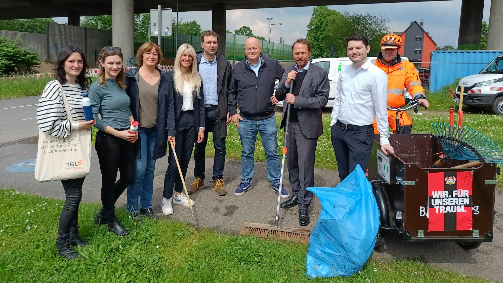 Vier Frauen und fünf Männer posieren zusammen für ein Foto. In den Händen halten sie Reinigungswerkzeuge.