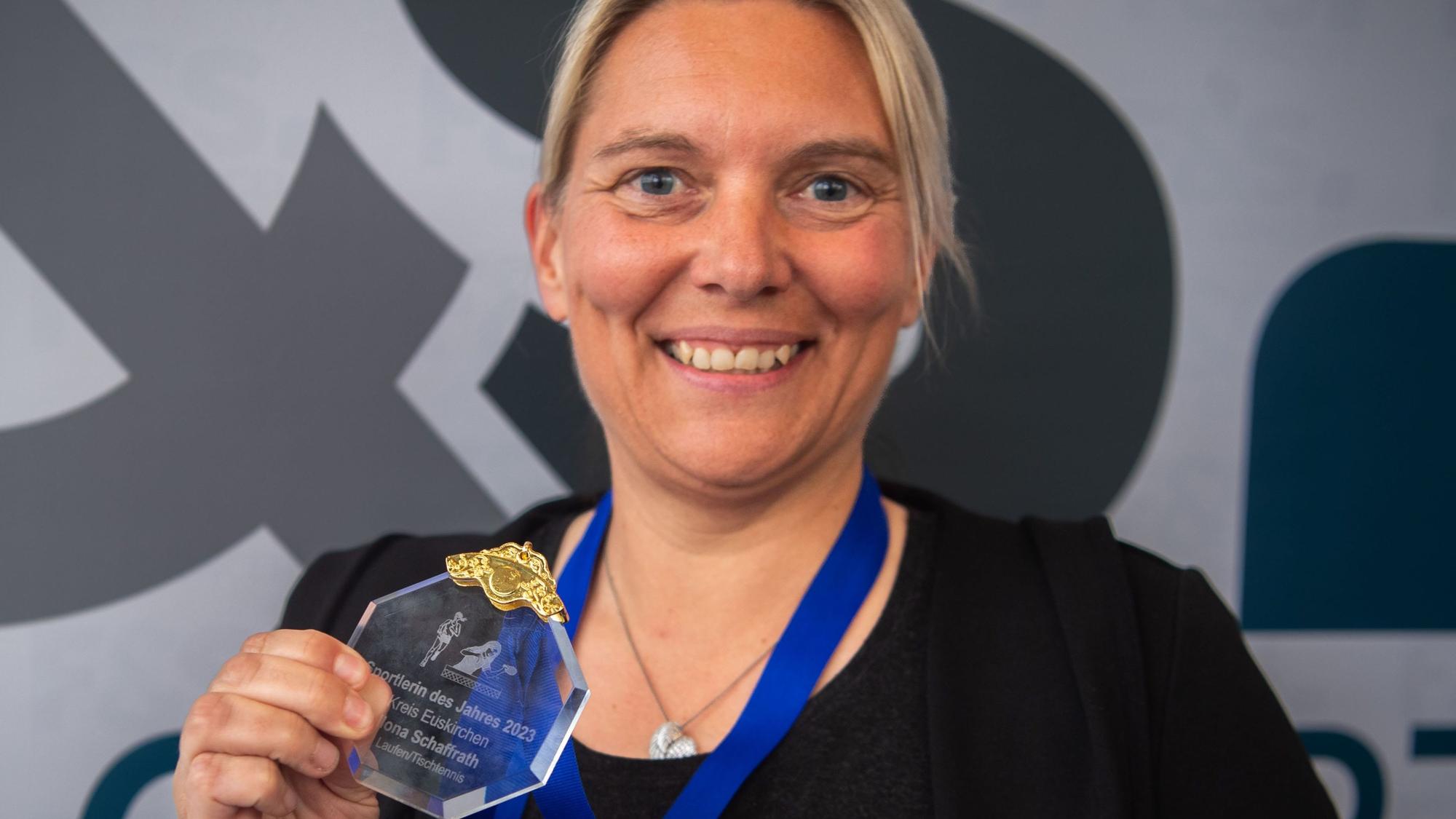 Ilona Schaffrath hält ihre Medaille in die Kamera und strahlt.