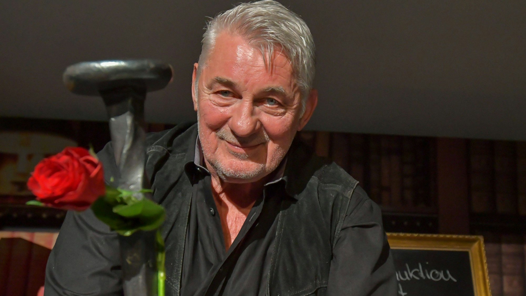 Heinz Hoenig trägt ein schwarzes Hemd und blickt in die Kamera.