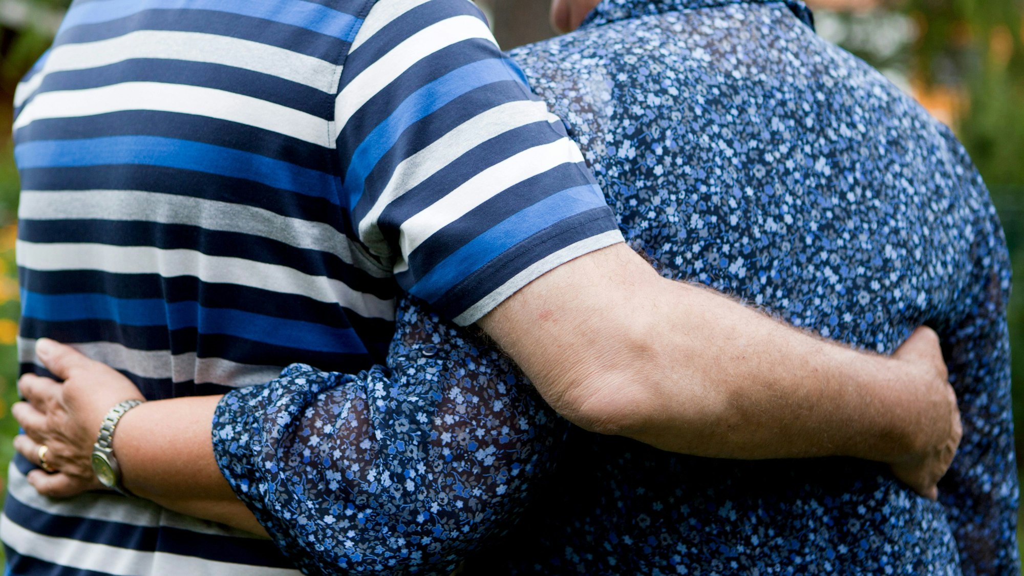 Ein älteres Paar geht enger Umarmung, man sieht ihre Oberkörper voon hinten.