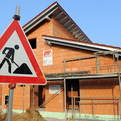 Ein Baustellenschild steht vor dem Rohbau eines Einfamilienhauses.