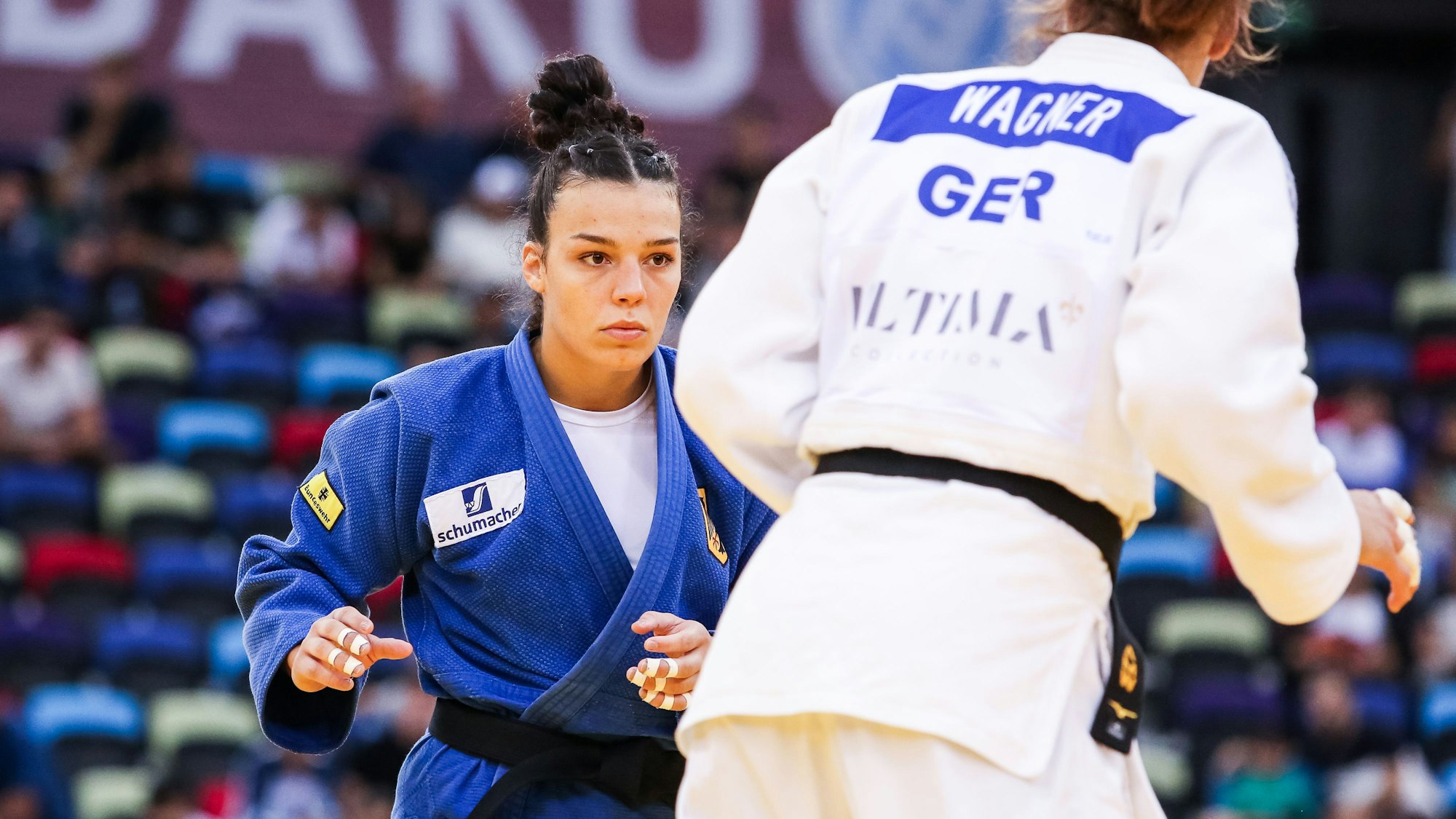 Die Judoka Alina Böhm und Anna-Maria Wagner während eines Kampfes. Böhm trägt einen blauen Judoanzug und ist von vorne zu sehen, Wagner trägt einen weißen Judoka und steht mit dem Rücken zur Kamera.